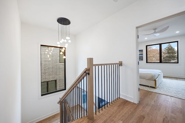 hall with baseboards, wood finished floors, an upstairs landing, a chandelier, and recessed lighting