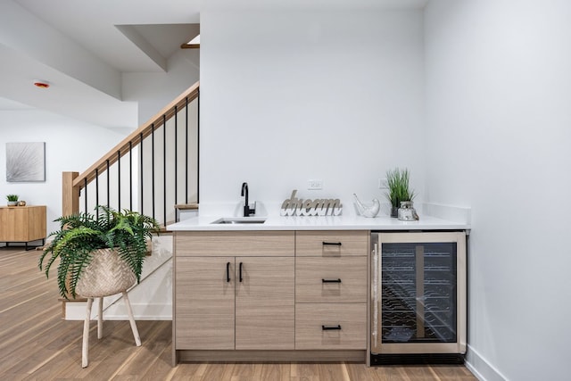 bar with beverage cooler, stairs, a sink, and light wood-style flooring