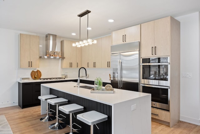 kitchen featuring stainless steel appliances, wall chimney range hood, and light brown cabinetry