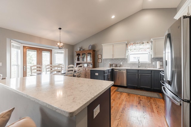 kitchen featuring light wood-type flooring, stainless steel appliances, decorative light fixtures, sink, and white cabinetry