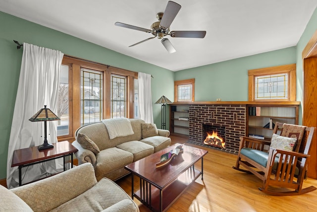 living room featuring ceiling fan, a brick fireplace, and light wood-style flooring