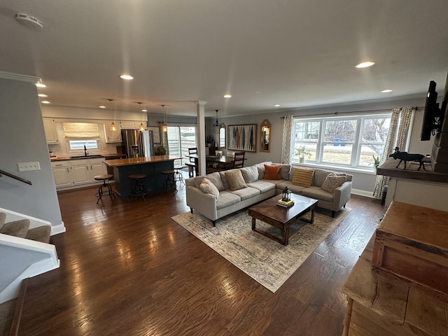 living room with sink, crown molding, dark wood-type flooring, and decorative columns