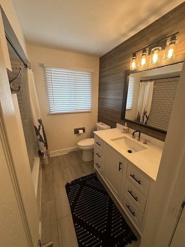 bathroom featuring vanity, toilet, and wood walls