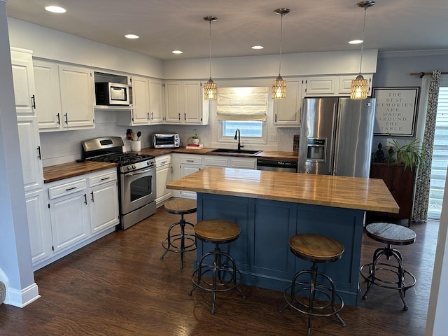 kitchen with hanging light fixtures, white cabinetry, appliances with stainless steel finishes, and butcher block counters