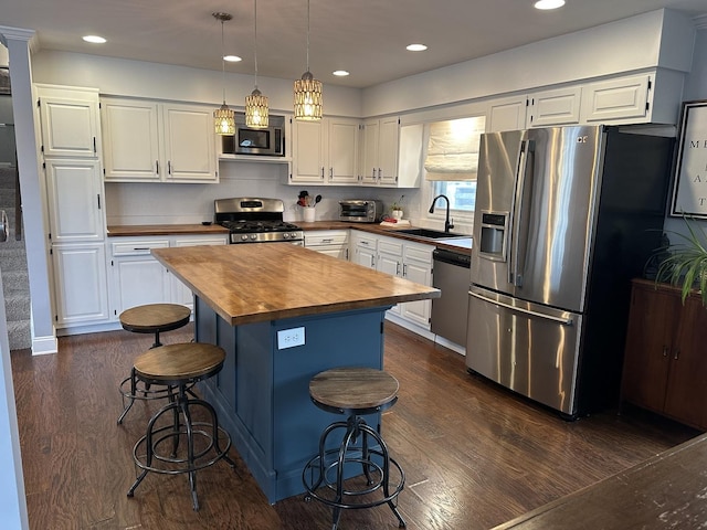 kitchen with sink, white cabinetry, hanging light fixtures, stainless steel appliances, and a center island