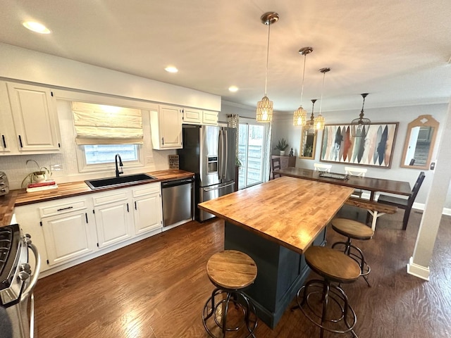 kitchen featuring pendant lighting, white cabinetry, stainless steel appliances, and butcher block counters