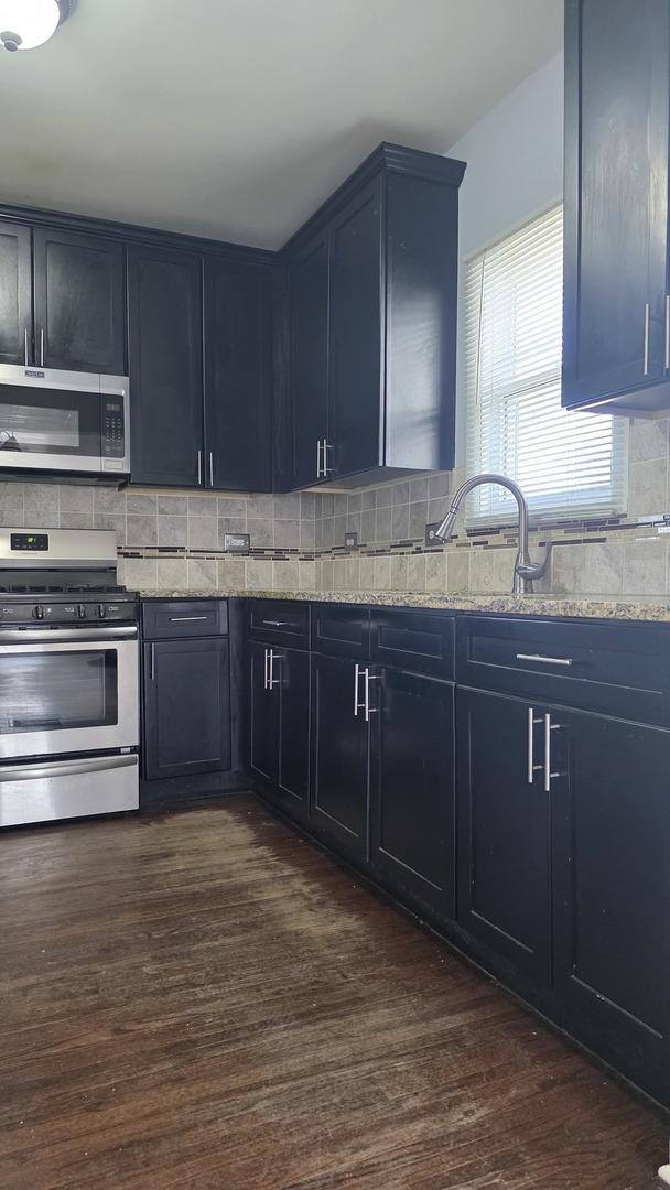 kitchen with tasteful backsplash, stainless steel appliances, dark hardwood / wood-style flooring, and light stone countertops