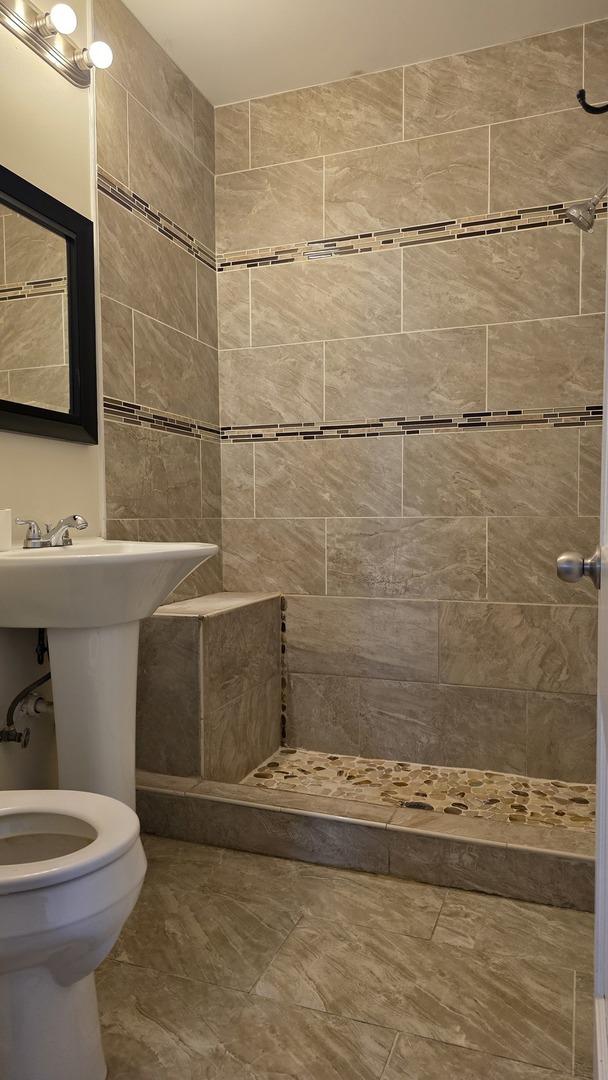 bathroom with tiled shower, sink, and toilet