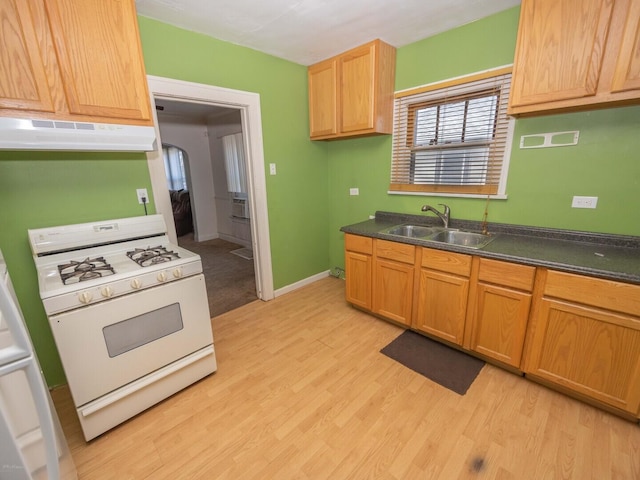 kitchen featuring dark countertops, white gas range oven, a sink, and under cabinet range hood