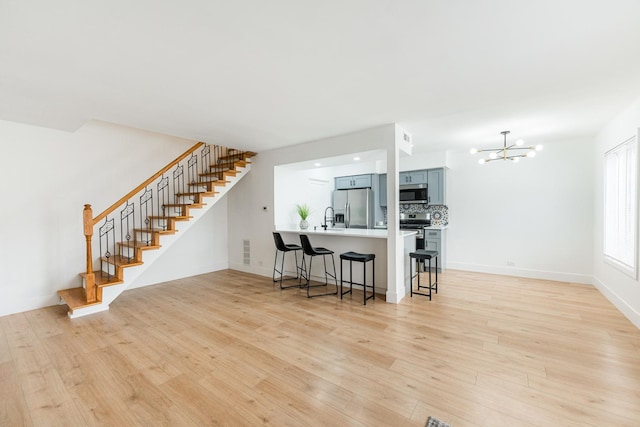 kitchen featuring appliances with stainless steel finishes, light wood-type flooring, a breakfast bar area, kitchen peninsula, and an inviting chandelier