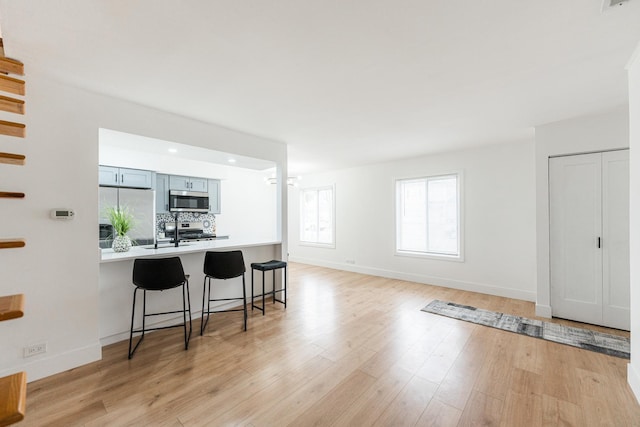 kitchen featuring tasteful backsplash, light hardwood / wood-style flooring, appliances with stainless steel finishes, a kitchen breakfast bar, and kitchen peninsula