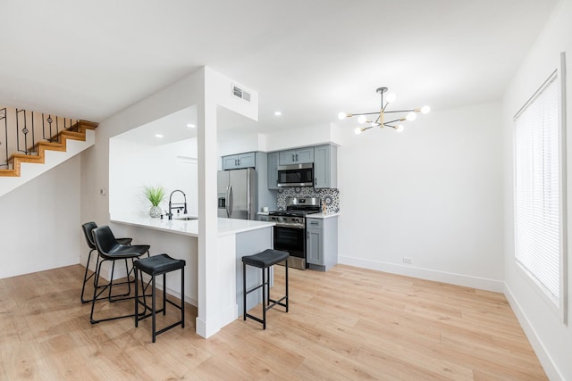 kitchen with gray cabinets, appliances with stainless steel finishes, a kitchen breakfast bar, a healthy amount of sunlight, and kitchen peninsula