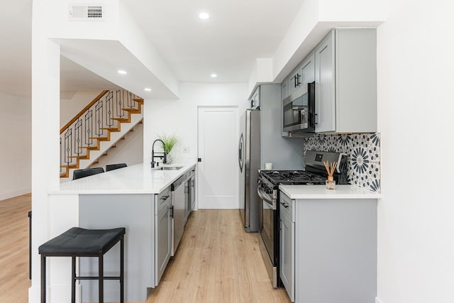 kitchen featuring a breakfast bar, sink, gray cabinetry, kitchen peninsula, and stainless steel appliances