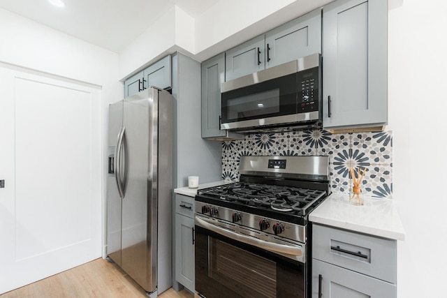 kitchen with tasteful backsplash, appliances with stainless steel finishes, light stone countertops, and light wood-type flooring