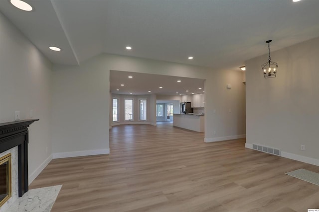 unfurnished living room featuring baseboards, light wood-style floors, a premium fireplace, and visible vents