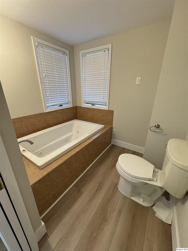 bathroom featuring tiled tub, hardwood / wood-style flooring, and toilet