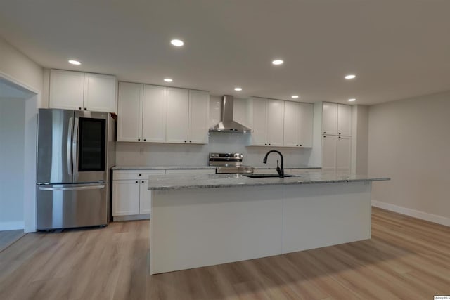 kitchen with wall chimney exhaust hood, stainless steel appliances, white cabinetry, a sink, and light wood-type flooring
