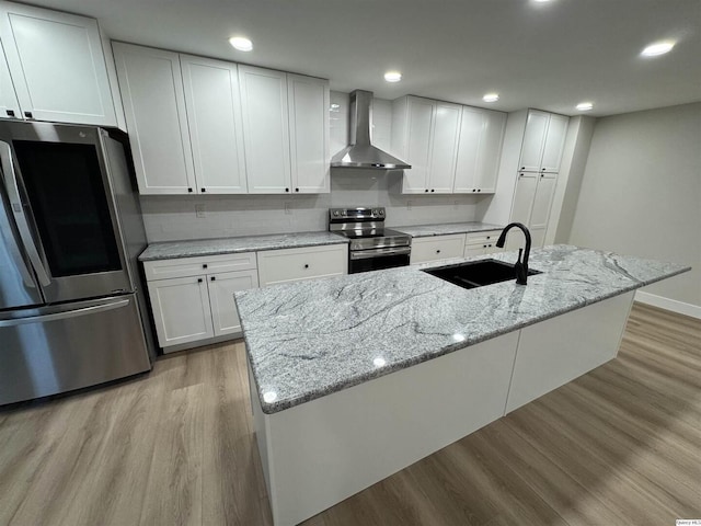 kitchen featuring sink, white cabinetry, light stone counters, appliances with stainless steel finishes, and wall chimney range hood