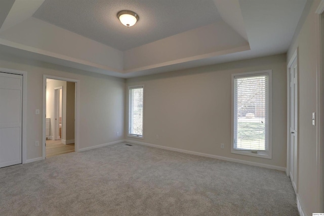 unfurnished bedroom with baseboards, a tray ceiling, and light colored carpet