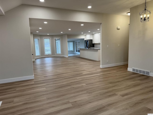 unfurnished living room with an inviting chandelier and light hardwood / wood-style flooring