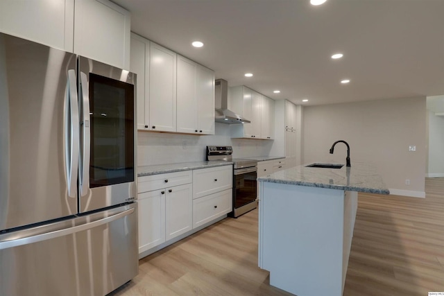 kitchen with white cabinetry, a sink, light wood-style flooring, appliances with stainless steel finishes, and wall chimney exhaust hood