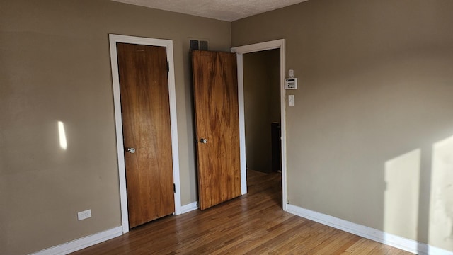 unfurnished bedroom featuring visible vents, a closet, baseboards, and wood finished floors