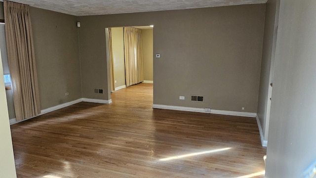 empty room featuring wood finished floors, visible vents, and baseboards