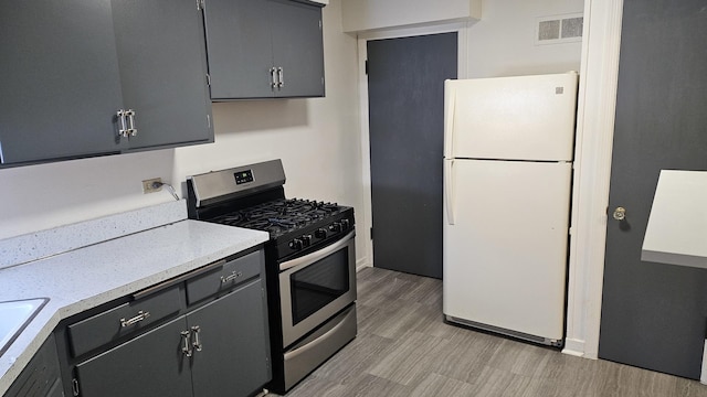 kitchen featuring freestanding refrigerator, gray cabinets, light countertops, and gas range