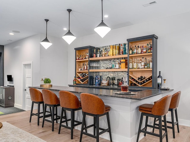 bar featuring decorative light fixtures, wet bar, light wood finished floors, and visible vents