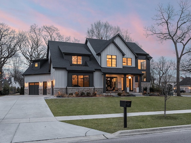 modern farmhouse style home featuring a front lawn, driveway, stone siding, and a shingled roof