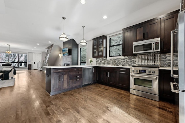 kitchen featuring stainless steel appliances, hanging light fixtures, dark brown cabinetry, and kitchen peninsula