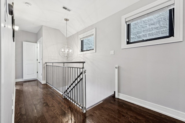 corridor with a notable chandelier, dark wood-type flooring, and vaulted ceiling