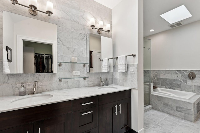 bathroom with vanity, a relaxing tiled tub, tile walls, and a skylight