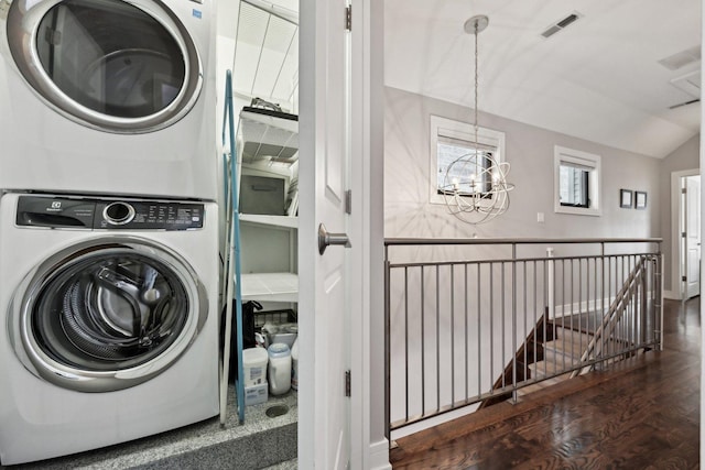 washroom featuring stacked washing maching and dryer, dark hardwood / wood-style floors, and a notable chandelier