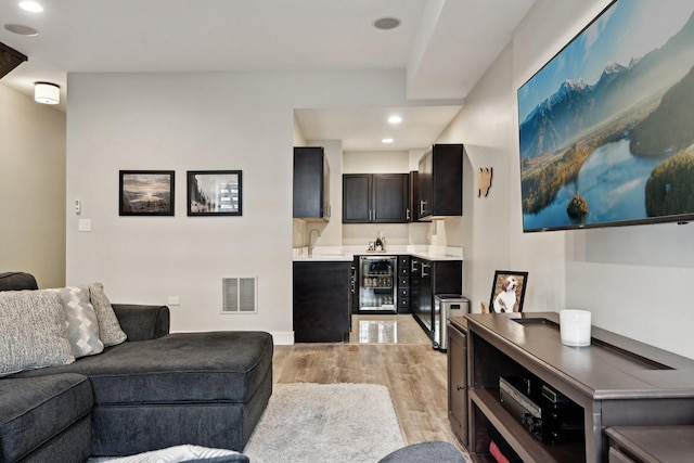 living room with sink, beverage cooler, and light hardwood / wood-style flooring