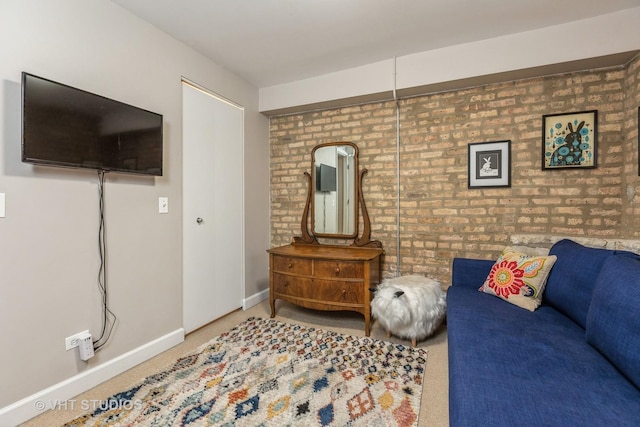 carpeted living area with brick wall and baseboards