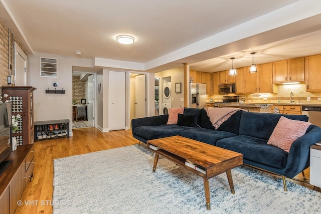 living room with stacked washer and dryer, baseboards, and light wood-style floors