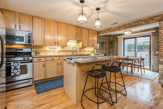 kitchen featuring light wood finished floors, stainless steel appliances, visible vents, a sink, and a kitchen island