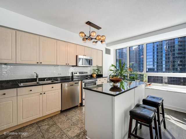 kitchen featuring dark countertops, stainless steel appliances, a sink, and decorative light fixtures