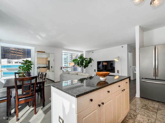 kitchen featuring open floor plan, dark stone countertops, light brown cabinets, and freestanding refrigerator