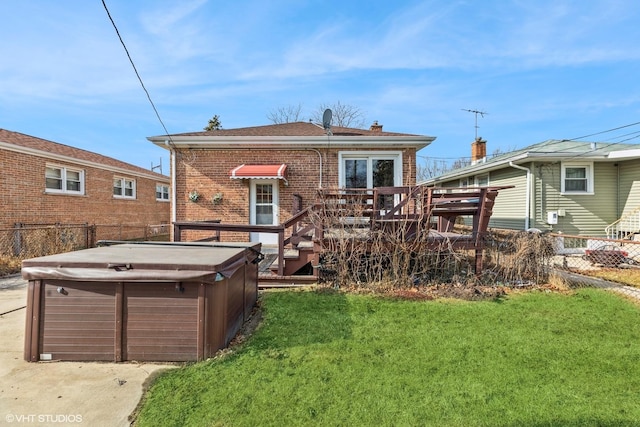 rear view of house featuring a hot tub, a deck, and a lawn