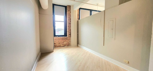 empty room featuring brick wall, wood finished floors, electric panel, and baseboards