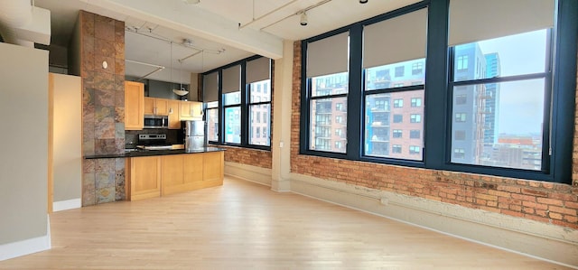 kitchen with dark countertops, hanging light fixtures, appliances with stainless steel finishes, light brown cabinets, and brick wall