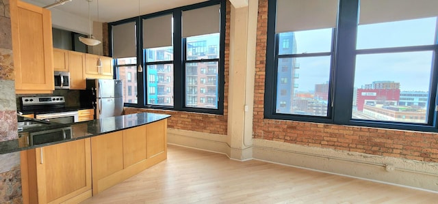 kitchen with pendant lighting, a city view, stainless steel appliances, brick wall, and dark stone countertops
