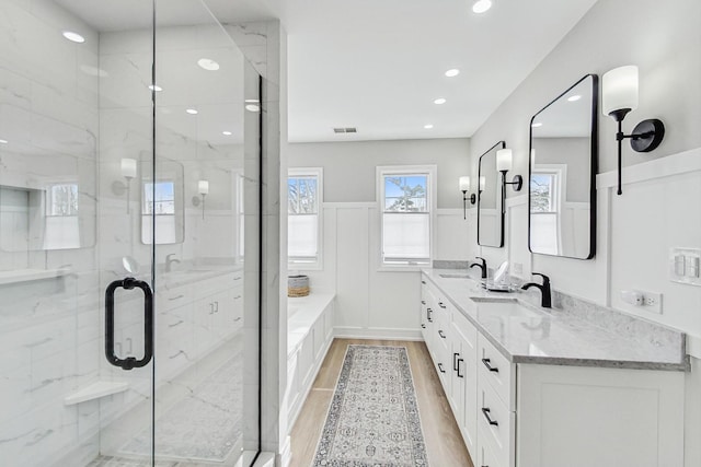 bathroom with visible vents, a wainscoted wall, wood finished floors, a shower stall, and a sink