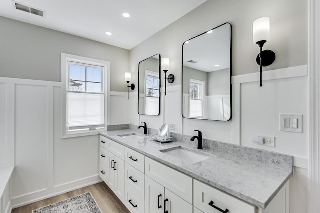 bathroom featuring double vanity, visible vents, a wainscoted wall, wood finished floors, and a sink