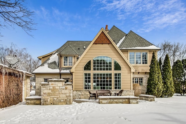 snow covered back of property featuring stone siding