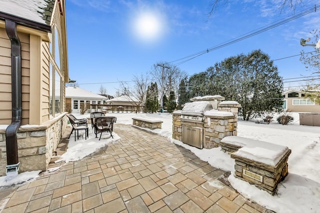 snow covered patio with outdoor dining space and grilling area