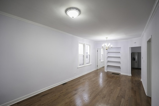 spare room with a notable chandelier, crown molding, dark wood-type flooring, and built in features