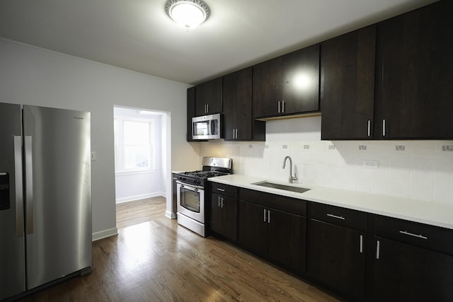 kitchen with appliances with stainless steel finishes, hardwood / wood-style floors, tasteful backsplash, sink, and dark brown cabinetry